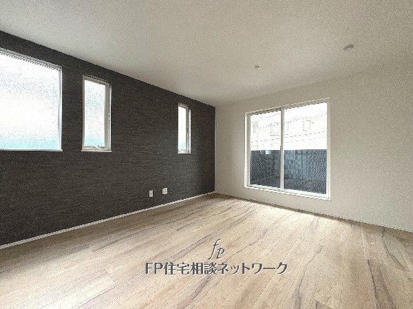 大きな窓から光が差し込む明るい空間。落ち着いた色合いのアクセントウォールが上質さを引き立て、家族が自然と集う、ぬくもりあふれるリビングです。