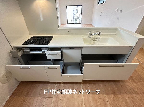 【キッチン収納】使い勝手の良いスライド収納が魅力のシステムキッチン。三口ガスコンロや広々としたシンクを備え、毎日の料理が快適に楽しめます。白と木目調の洗練されたデザインが、上質な暮らしを演出。