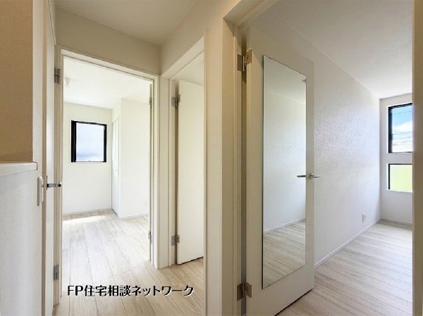 【2階廊下】  白を基調とした清潔感あふれる内装が魅力です。建具には便利な姿見が備え付けられており、お出かけ前のチェックもスムーズ。窓からの自然光が、明るく心地よいプライベート空間を演出します。