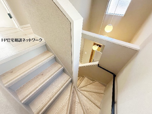 玄関扉を開けた瞬間に広がる、開放感あふれる吹抜けの階段スペース。高窓から降り注ぐ自然光がエントランス全体を明るく照らし、ペンダントライトの柔らかな灯りが訪れる人を優しく迎える、印象的な空間です。