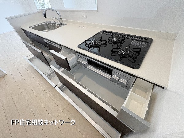 【キッチン】  使い勝手の良いスライド収納が魅力のシステムキッチン。三口ガスコンロや広々としたシンクを備え、毎日の料理が快適に楽しめます。白と木目調の洗練されたデザインが、上質な暮らしを演出。