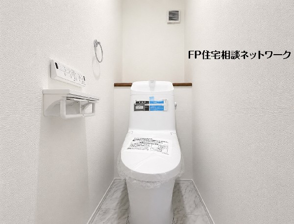 【トイレ】清潔感に満ちた白を基調としたトイレです。多機能な温水洗浄便座のリモコンが壁に設置され、ペーパーホルダーも複数用意。床は大理石調で高級感があり、快適な空間です。